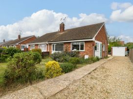 A single-story brick house with a tiled roof a front garden with shrubs and a gravel driveway leading to a garage at Little Lodge in Dersingham