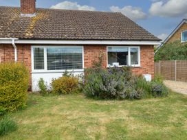 A brick house with two windows and bushes in front with a grassy lawn at Little Lodge in Dersingham