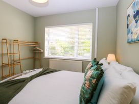 A bedroom with a bed with floral pillows a wooden clothes rack and a window with blinds at Little Lodge in Dersingham