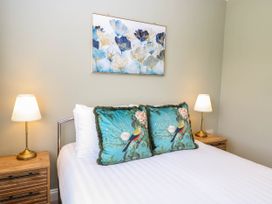 A bedroom with a bed featuring two bird-themed pillows two bedside tables with lamps and floral artwork above the headboard at Little Lodge in Dersingham