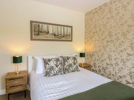 A bedroom with a bed with palm tree patterned pillows two bedside tables with lamps and a painting of a forest above the bed at Little Lodge in Dersingham