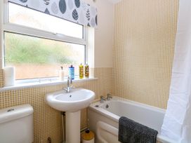 A bathroom with a pedestal sink, a bathtub with a towel hanging on the side, a toilet, and a window with frosted glass and patterned curtains at Little Lodge in Dersingham