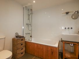 A bathroom featuring a toilet, bathtub with shower, and storage basket at Coombe Barn in Cusgarne near St Day