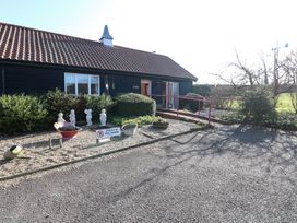 A building with a tiled roof and dark exterior with a ramp leading to the entrance surrounded by bushes and garden ornaments at Swallow Barn in Holton near Halesworth