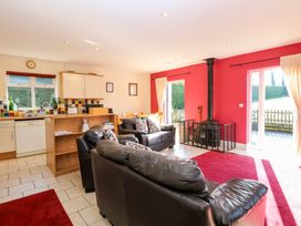 An open living area with black leather sofas a wood stove with protective screen red walls and an adjacent kitchen with tiled backsplash and white cabinets at Swallow Barn in Holton near Halesworth