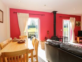 A dining area with wooden table and chairs next to a living room with a black leather sofa and a wood stove in front of red walls at Swallow Barn in Holton near Halesworth