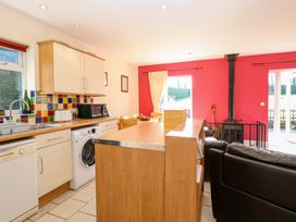 A kitchen and dining area with wooden cabinets colorful tiled backsplash a washing machine a wood stove and black couches at Swallow Barn Holton near Halesworth
