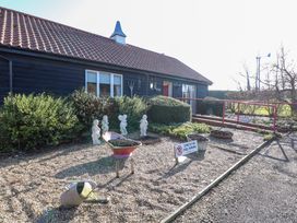 An exterior view of a building with a tiled roof and black wooden siding with garden statues bushes wheelbarrow and watering can in front at Swallow Barn Holton near Halesworth