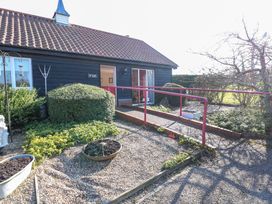 Exterior view of a building with a tiled roof and black wooden walls with bushes and a gravel path with a red handrail at Swallow Barn Holton near Halesworth