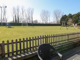 A fenced grass playground with a goalpost swing set and a wooden playhouse at Swallow Barn in Holton near Halesworth