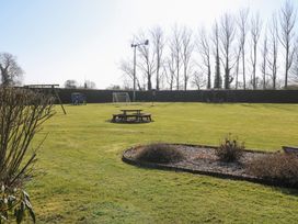 A large green lawn with a picnic table, playground equipment, a soccer goal, and a covered seating area at Swallow Barn in Holton near Halesworth