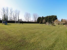 A large grassy field with a playhouse slide, soccer goal, swings, and picnic tables surrounded by trees at Swallow Barn in Holton near Halesworth