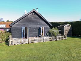 A fenced backyard with a wooden shed and black wooden house at Swallow Barn in Holton near Halesworth