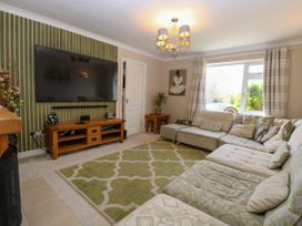 A living room with a large wall-mounted TV wooden TV stand green and beige patterned rug sectional sofa and window with plaid curtains at 6 Barleycroft in Hemsby