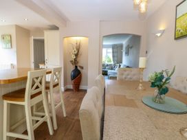 A dining area with chairs and a table with a candle and flowers a kitchen island with stools and a living room visible through an arch at 6 Barleycroft in Hemsby