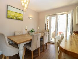 A dining room with a wooden table and beige upholstered chairs with glass doors leading outside at 6 Barleycroft in Hemsby