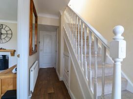 A hallway with a wooden floor radiator white door and carpeted stairs with white railing at 6 Barleycroft in Hemsby