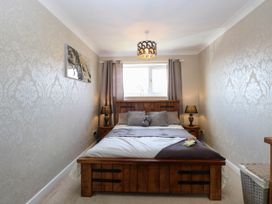 A bedroom with a wooden bed frame bedside tables with lamps a window with curtains and patterned wallpaper at 6 Barleycroft in Hemsby