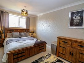 A bedroom with a wooden bed frame bedside tables lamps a wooden dresser a laundry basket and a framed picture on the wall at 6 Barleycroft in Hemsby