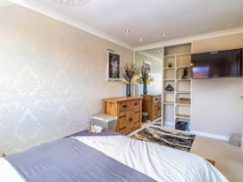 A bedroom with a bed covered by blankets a wooden dresser a wall-mounted television and a mirrored sliding door wardrobe at 6 Barleycroft in Hemsby