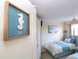 A bedroom with two single beds with blue and white bedding a framed sea horse decoration on the wall and a painting of a beach at 6 Barleycroft in Hemsby