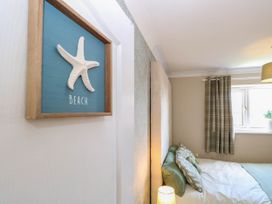 A bedroom with a bed with green and white pillows a window with checkered curtains and a framed starfish on a wall 6 Barleycroft in Hemsby