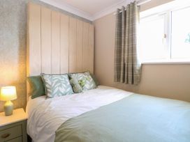 A bedroom with a bed with green and white bedding next to a window with plaid curtains and a bedside table with a lamp at 6 Barleycroft in Hemsby