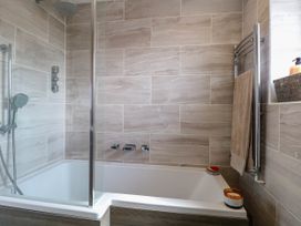 A bathtub with a shower and a glass screen next to a towel rack in a bathroom at 6 Barleycroft in Hemsby