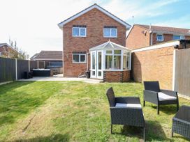 A backyard with a grassy lawn a conservatory and outdoor seating at 6 Barleycroft in Hemsby