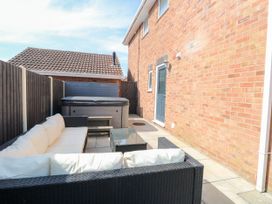 An outdoor patio area with a hot tub a black wicker sofa with white cushions and a glass coffee table at 6 Barleycroft in Hemsby