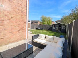 A backyard with a patio area featuring a cushioned outdoor sofa and table a lawn with garden furniture and a shed at 6 Barleycroft in Hemsby