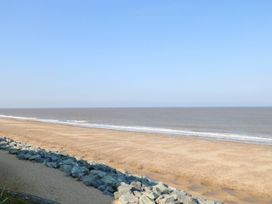A sandy beach with rocks along the shore and calm sea under a clear sky at 6 Barleycroft in Hemsby