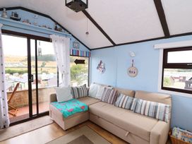 A living room with a beige sectional sofa with striped cushions near sliding glass doors and windows at Captains Cabin in Clarach Bay near Aberystwyth