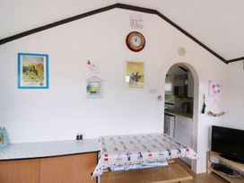 A dining area with a table covered by a nautical-themed cloth and a bench under an arched doorway leading to a kitchen at Captains Cabin in Clarach Bay near Aberystwyth