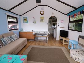 A living room with a beige sofa a TV on a wooden stand a small table with a cover and cushions at Captain's Cabin in Clarach Bay near Aberystwyth