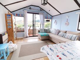 A living room with a beige sectional sofa striped cushions a wooden cabinet a heater and a glass door leading to a balcony at Captain's Cabin Clarach Bay near Aberystwyth