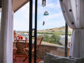 A balcony with wooden chairs and table set with teapots and mugs overlooking a landscape at Captain's Cabin in Clarach Bay near Aberystwyth