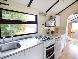 A kitchen with a sink a gas stove a microwave a kettle and cups hanging on the wall at Captains Cabin in Clarach Bay near Aberystwyth