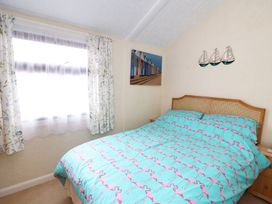 A bedroom with a bed covered in flamingo bedding beside a window with floral curtains at Captains Cabin in Clarach Bay near Aberystwyth