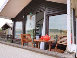 A small outdoor seating area with two wooden chairs a round table a red teapot and a striped mug at Captain's Cabin in Clarach Bay near Aberystwyth