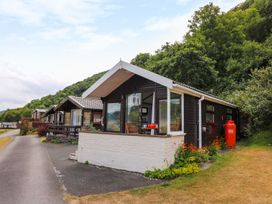 A row of holiday cabins next to a road with trees and hills in the background at Captain's Cabin in Clarach Bay near Aberystwyth