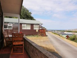 A patio with wooden chairs and a table next to a brown cabin and a road leading to other cabins at Captain's Cabin Clarach Bay near Aberystwyth