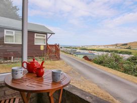 A wooden table with a red teapot red jug and two mugs on a patio overlooking a road and houses at Captain's Cabin in Clarach Bay near Aberystwyth