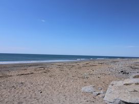 A sandy beach with scattered rocks and calm sea under a clear blue sky at Captains Cabin Clarach Bay near Aberystwyth