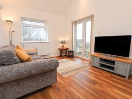 A living room with a gray sofa and yellow pillows a wooden floor a TV on a stand a small electric fireplace and a window with a view at Meadow Cottage in Staintondale near Cloughton