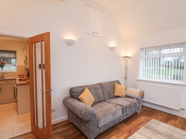 A living room with a gray sofa and yellow cushions next to a window with vertical blinds at Meadow Cottage in Staintondale near Cloughton