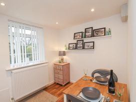 A dining area with a wooden table set for two near a window with blinds and a small chest of drawers with a lamp and framed pictures on shelves at Meadow Cottage in Staintondale near Cloughton