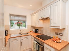 A kitchen with white cabinets wooden countertops a sink under a window flowers on the windowsill and breakfast items on the counter at Meadow Cottage in Staintondale near Cloughton