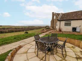 An outdoor patio area with a round table and four chairs next to a house overlooking fields and trees at Meadow Cottage in Staintondale near Cloughton