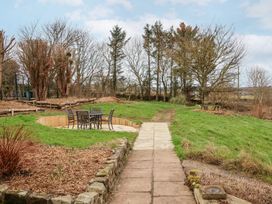 A garden with a paved walkway leading to a patio area with a table and chairs and trees in the background at Meadow Cottage in Staintondale near Cloughton